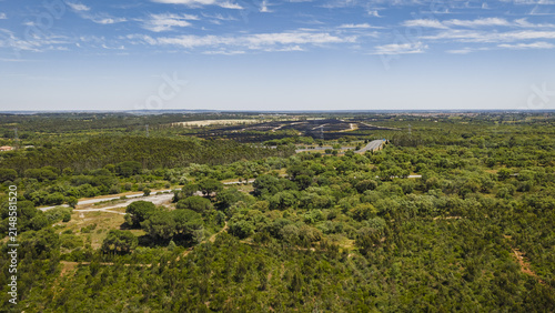 Aerial view of the lush green landscape in Santarem, featuring dense forests, rolling hills, and a winding road under a bright blue sky in Santarem, Santarem District, Portugal.