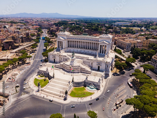 Aerial view of Monument to Victor Emmanuel II surrounded by historic urban architecture, stone plazas, and lush green trees in Roma, Lazio, Italy.