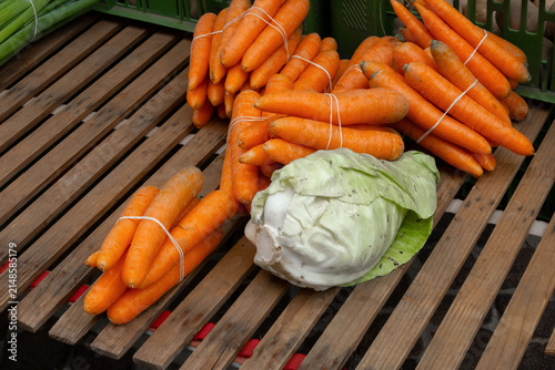 Freshly harvested orange carrots bundled with white string alongside a green cabbage on a wooden surface in a market setting