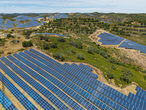Aerial view of a large-scale solar farm with rows of photovoltaic panels installed across the rolling hills of the countryside in Vaqueiros, Faro District, Portugal.