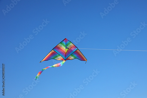 Foto Colorful rainbow delta kite flying high in clear blue sky