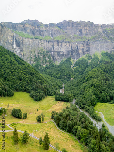 View of the dramatic limestone cliffs and cascading waterfalls of Cirque du Fer a Cheval surrounded by lush green forests and mountain meadows in Sixt-Fer-a-Cheval, Auvergne-Rhone-Alpes, France.