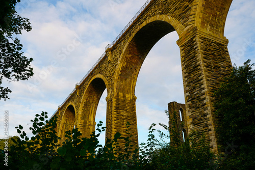 The historic Moorswater Viaduct near Liskeard, Cornwall, spans a deep valley with eight striking semi-circular arches built from snecked rock-faced slatestone and granite. 