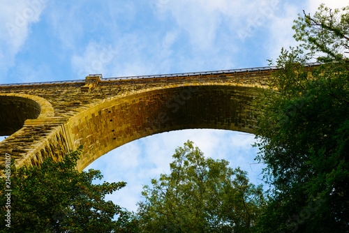 The historic Moorswater Viaduct near Liskeard, Cornwall, spans a deep valley with eight striking semi-circular arches built from snecked rock-faced slatestone and granite. 