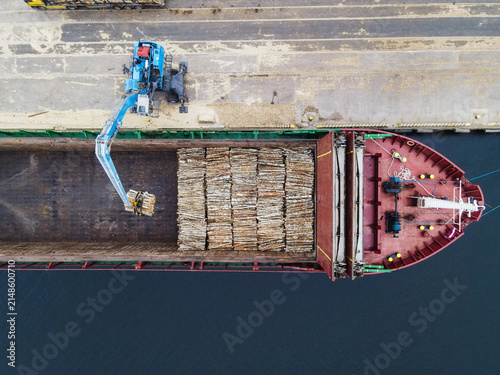 Aerial view of a cargo ship being loaded with timber logs by a crane at the port in Riga, Latvia.