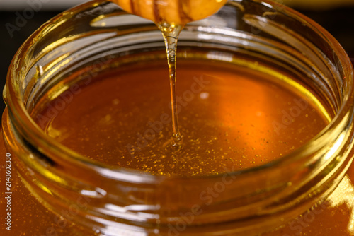 Honey dripping from a wooden honey dipper in a jar