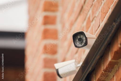 Security surveillance cameras mounted on a red brick wall monitoring public area, modern video security system protecting property, infrastructure and urban environment with continuous observation
