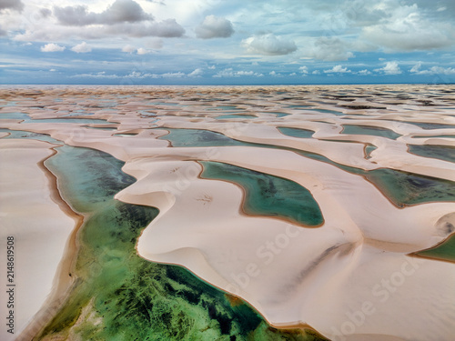 Aerial view of Lagoa Bonita featuring white sand dunes and turquoise lagoons under a cloudy sky in Barreirinhas, Maranhao, Brazil.