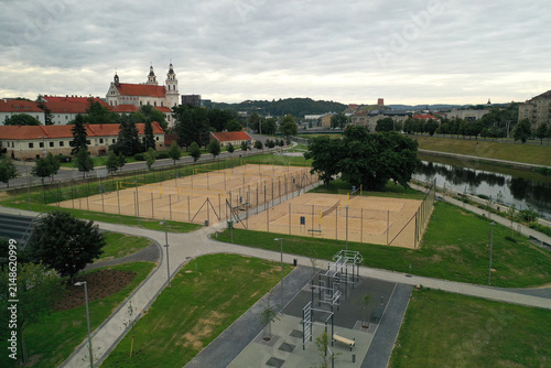 Aerial view of sand volleyball courts and a fitness area near the Neris River with the Church of St. Philip and St. James in the background in Lithuania.