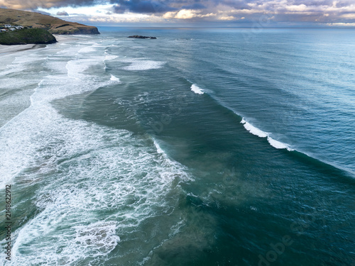 Aerial view of the coastline with rolling waves breaking on the sandy beach under a cloudy sky in Dunedin, Otago Region, New Zealand.
