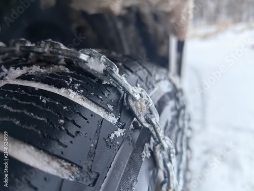 Close-up macro of snow chains fitted on a car tire covered in snow and ice. Winter car equipment and driving safety concept on icy road conditions.
