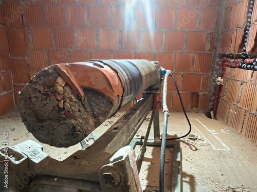Horizontal diamond core drilling machine with a extracted concrete and brick core sample inside the bit. Professional heavy-duty drilling process on an under-construction site.