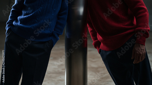 Two Men in Blue and Red Sweaters Leaning Against Pillar