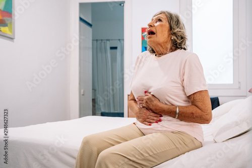 Senior woman experiencing stomach pain and indigestion in bedroom
