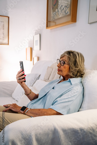 Senior woman relaxing on sofa using smartphone