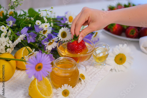 A ripe juicy strawberry is slowly coated in smooth honey while bright lemons and white flowers create a fresh seasonal composition. Natural sweetness and elegant food styling.