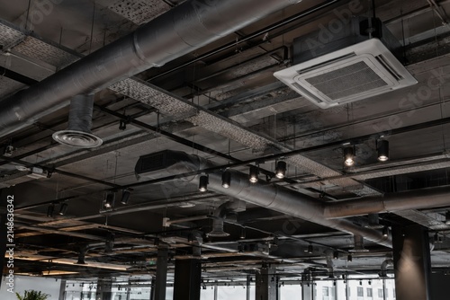  Techo de estilo industrial expuesto con conductos de ventilación metálicos, sistema de aire acondicionado y luces modernas en un espacio comercial