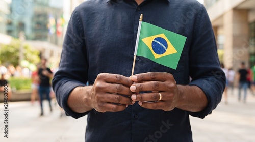 Close-up de mãos segurando pequena bandeira brasileira em ambiente moderno com fundo desfocado, conceito elegante para campanhas da Independência do Brasil