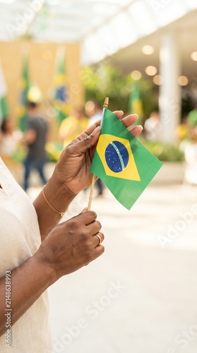 Close-up de mãos segurando pequena bandeira brasileira em ambiente moderno com fundo desfocado, conceito elegante para campanhas da Independência do Brasil