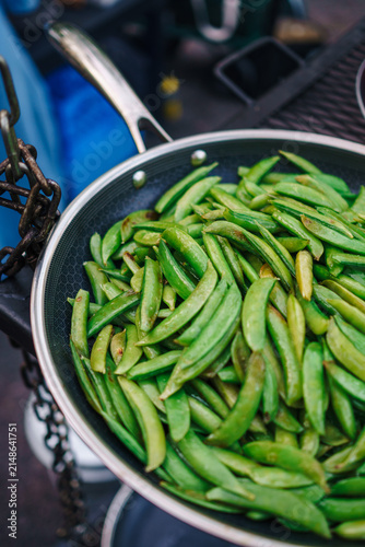 A pan full of green beans cooking over a fire on an outdoor cooker