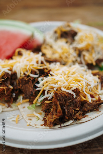 Pulled pork tacos with shredded cheese on top with watermelon in the background at a barbecue