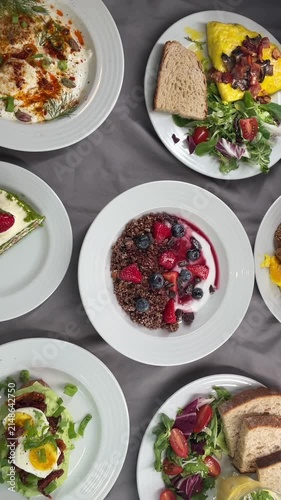 direct overhead view of plated breakfast spread featuring granola yogurt bowl with strawberries and blueberries, alongside omelet, bread, salad, and dairy sides