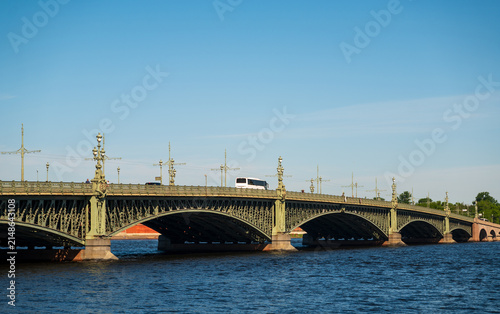 View of the ornate metal arches and decorative lampposts of the historic Trinity Bridge spanning the Neva River in Saint Petersburg, Russia.
