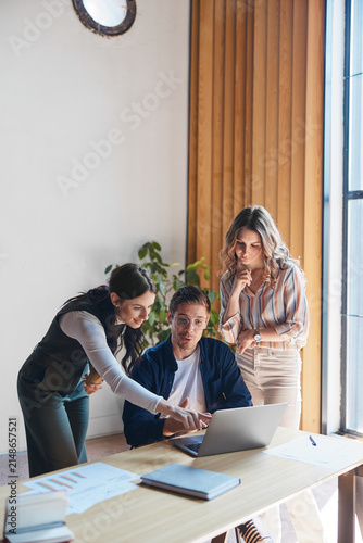 Diverse business professionals actively collaborating around a laptop. A female colleague pointing at the screen during a focused discussion