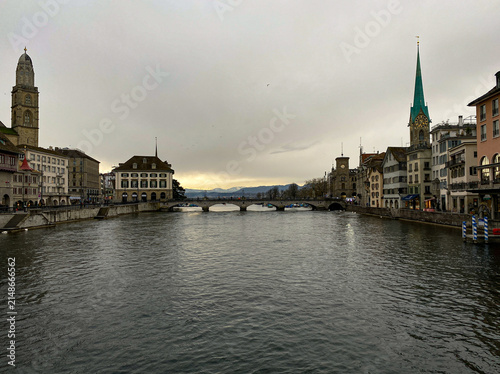 View of the Limmat river flowing through the historic city center of Zurich with the Grossmunster and Fraumunster churches under a cloudy sky in Zurich, Zurich, Switzerland.