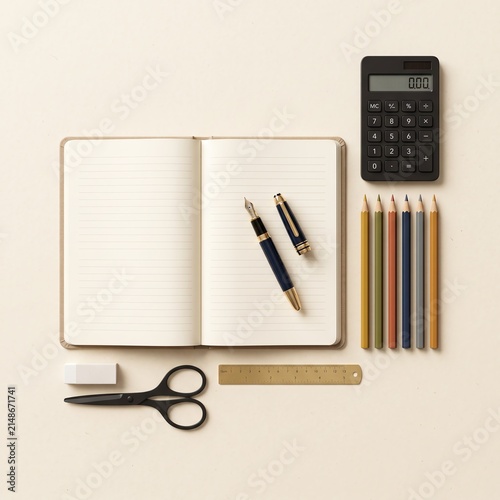 Flat lay of an open planner with a fountain pen calculator colored pencils and office supplies on beige