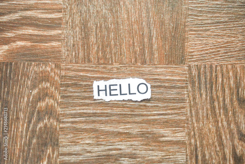 Fotografie The word HELLO printed on a piece of torn white paper, placed on a brown parquet wooden surface