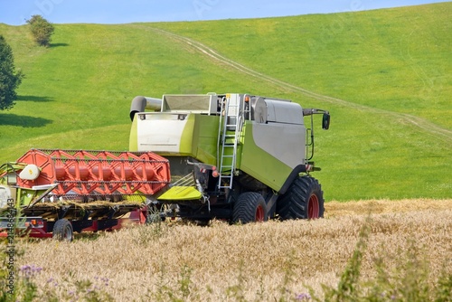 Combine harvester rear view in wheat field with green hills background