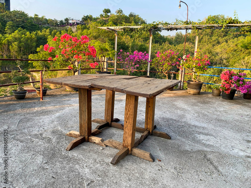 Rustic wooden table on an outdoor concrete rooftop terrace surrounded by colorful potted bougainvillea flowers.