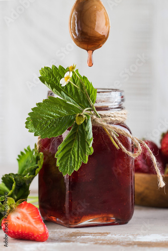 Homemade strawberry jam in a glass jar with fresh berries and honey drizzle