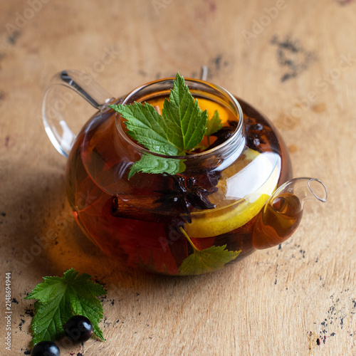 Glass teapot with herbal tea, lemon, mint and spices on wooden table