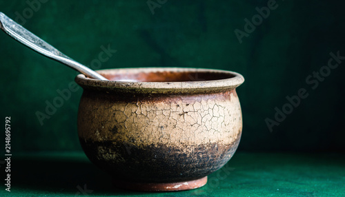 Rustic Ceramic Pot with Spoon on Green Background.