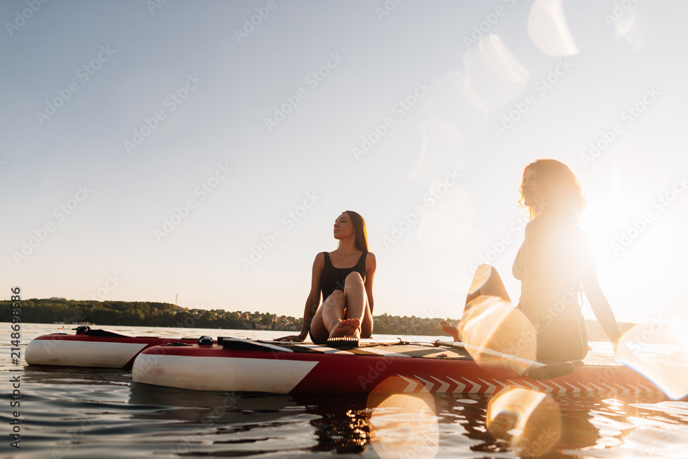 Fototapeta premium Women paddleboarding relaxing on water at sunset
