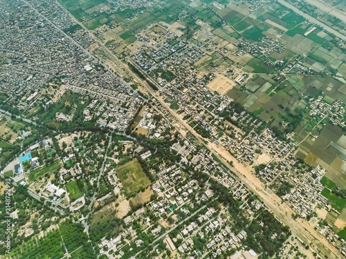 Aerial view of the urban landscape of Dera Ghazi Khan, featuring dense residential blocks, intersecting roads, and surrounding agricultural fields in Dera Ghazi Khan, Punjab, Pakistan.