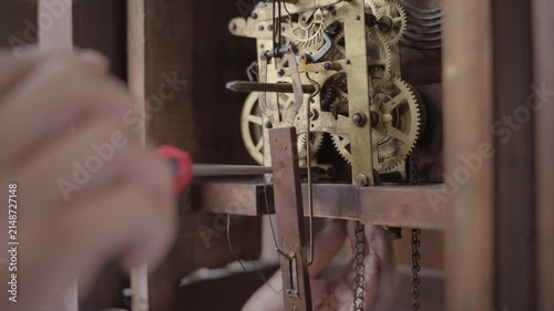Profile close up shot of a watchmaker using a precision manual screwdriver to adjust and tighten gears inside an antique mechanical grandfather clock.