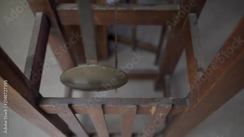 High angle close up shot looking down at a long wooden pendulum with a large brass disc swinging inside a vintage wood and brass Mission style grandfather clock.