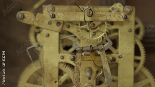 Macro front view shot of a brass mechanical gear ticking and rotating rhythmically inside the internal movement mechanism of a vintage antique grandfather clock.