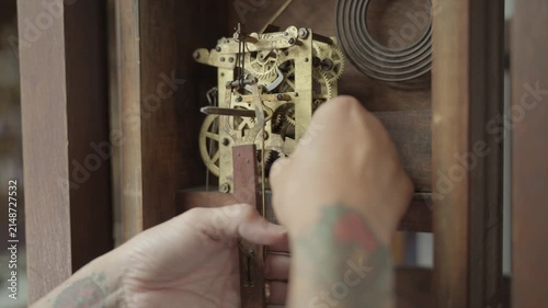 Close up shot of a watchmaker carefully removing the brass mechanical movement and gears from an antique grandfather clock during a restoration process.