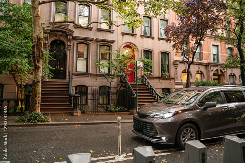 Foto Wide view of classic New York brownstone townhouses along a tree lined residential street with parked car in the foreground