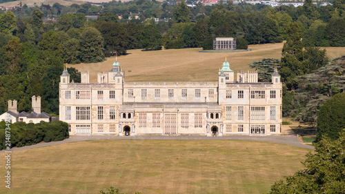 Aerial view of Audley End House, a grand Jacobean mansion, set within expansive lawns and surrounded by lush trees under a clear sky Audley End, England, United Kingdom.