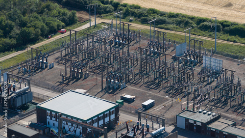 Aerial view of the electrical substation with metal structures, transformers, and power lines, surrounded by green fields and trees in Bishops Stortford, England, United Kingdom.