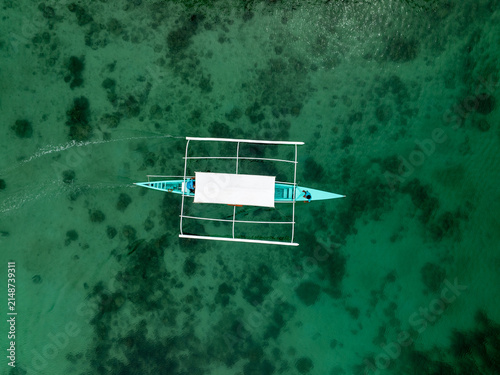 Aerial view of a traditional outrigger boat gliding through the clear turquoise waters of Sugba Lagoon in Del Carmen, Caraga, Philippines.