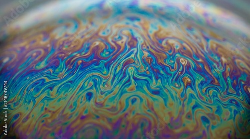 Abstract macro photography of a soap bubble surface with swirling iridescent colors.