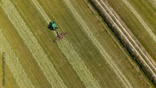 Aerial view of a tractor with a tedder attachment working in a field, turning and spreading freshly cut hay to improve drying in the summer sun in Milan, Lombardy, Italy.