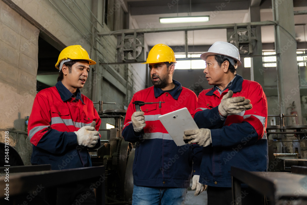 Fototapeta premium Senior engineer leading technician team using tablet to inspect and discuss heavy machinery maintenance in factory.