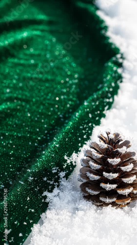 Frosty Pine Cone Resting on White Snow Beside Sparkling Green Fabric for Christmas Decoration